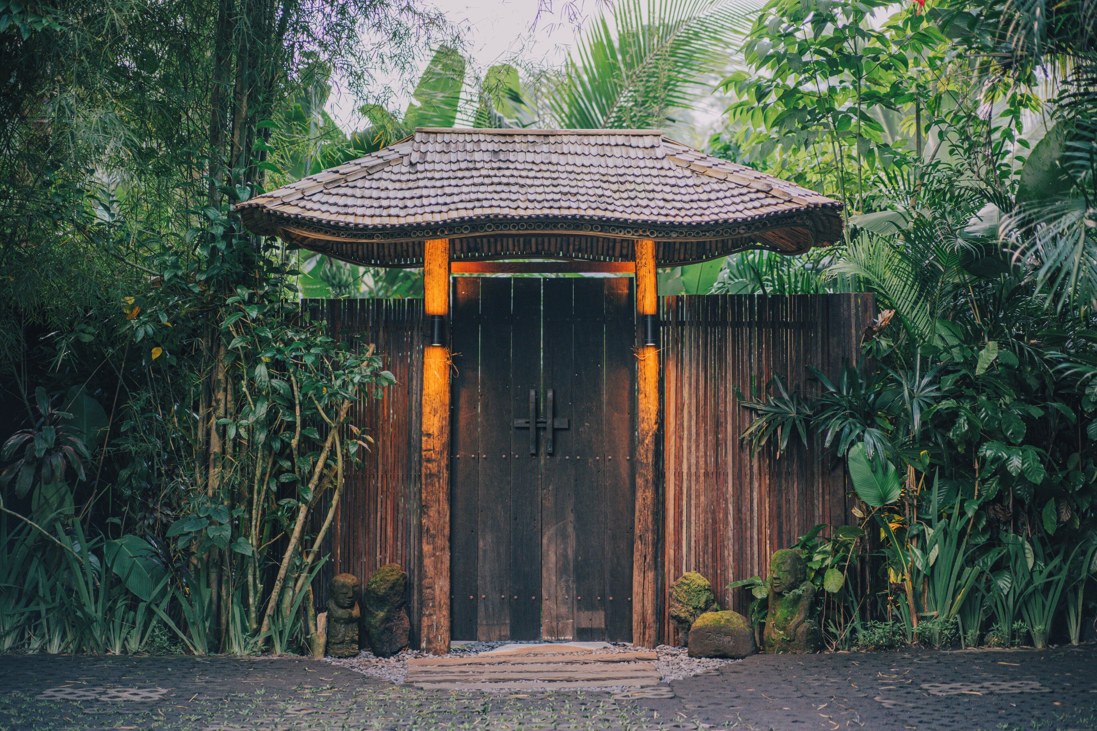 Una puerta de madera tradicional con techo de tejas, rodeada de exuberante vegetación tropical.