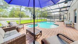 An outdoor pool area with lounge chairs, a table, and a blue umbrella. - Affordable Luxury 4 BR Villa, Close to Disney & Orlando, Pool/Spa, Arcade Games. (Clermont)