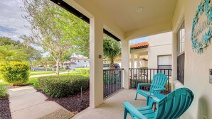 A covered outdoor area with two turquoise chairs and a table, a small garden, and a view of neighboring houses. - Affordable Luxury 4 BR Villa, Close to Disney & Orlando, Pool/Spa, Arcade Games. (Clermont)