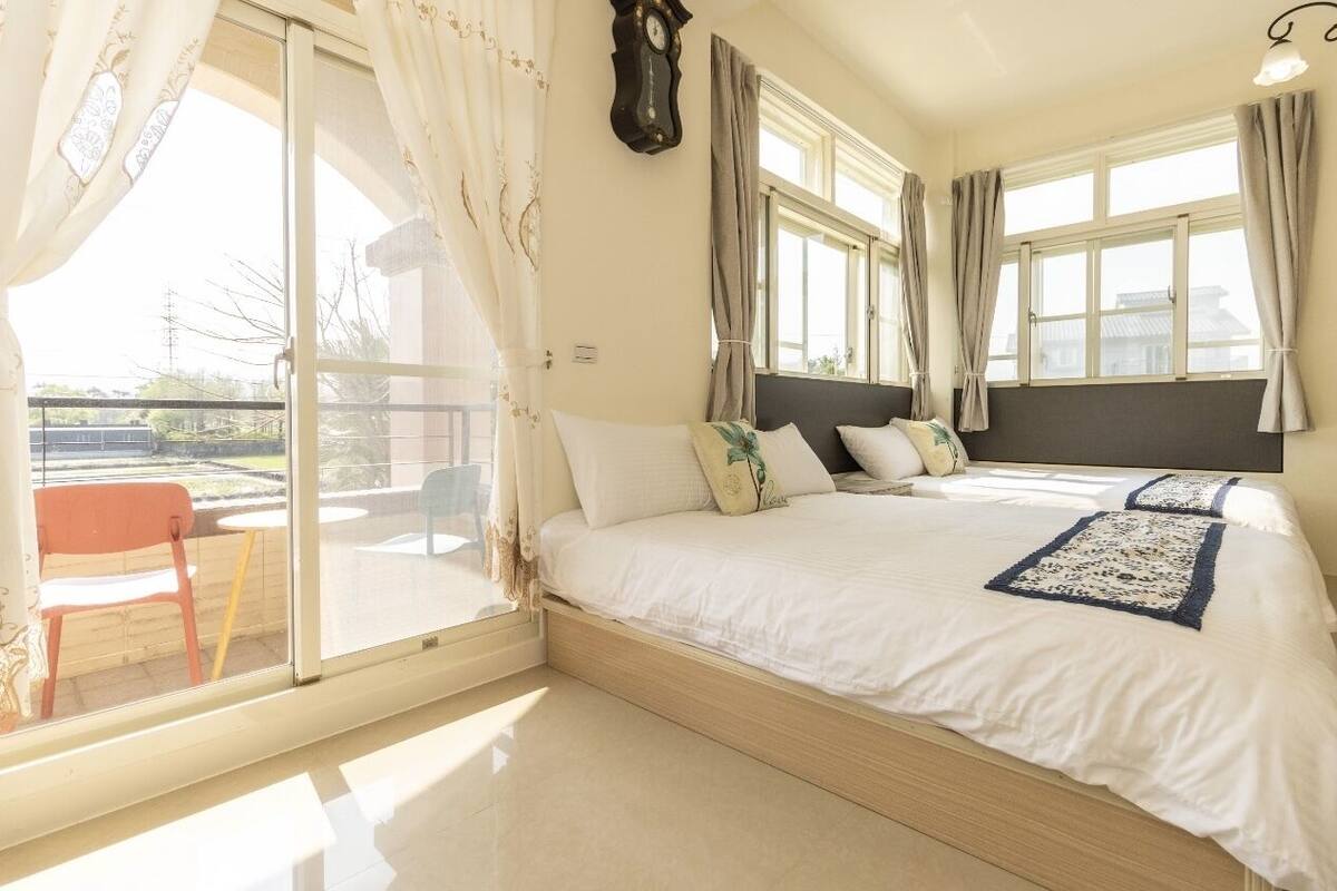 A bedroom with a large bed, a sliding glass door to a balcony, and a clock on the wall.