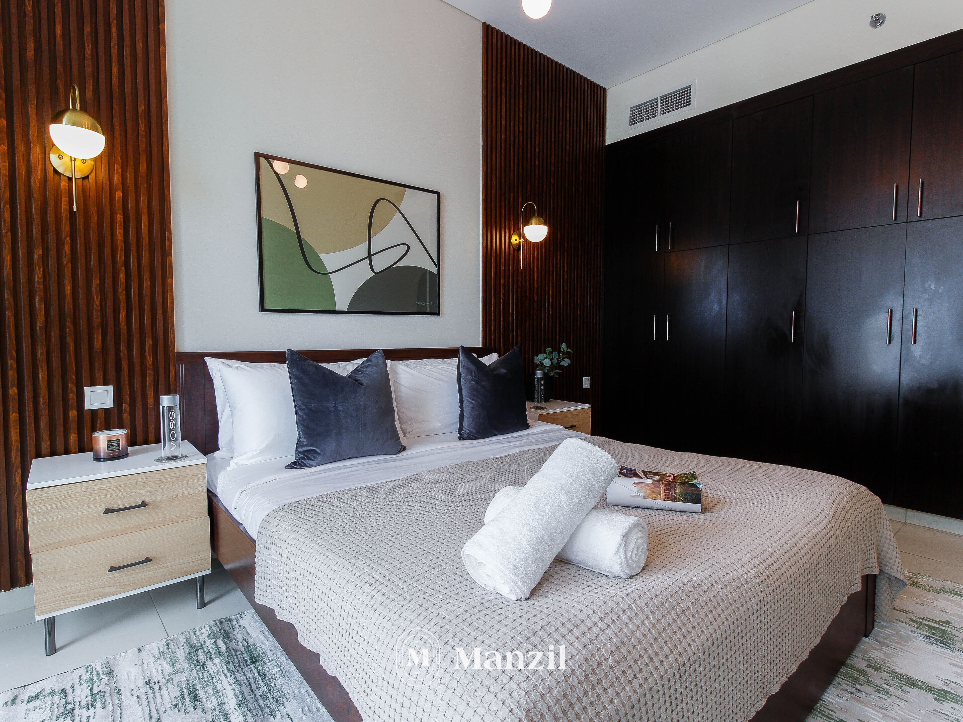 A modern bedroom with a large bed, dark wooden wardrobe, and a contemporary abstract painting.