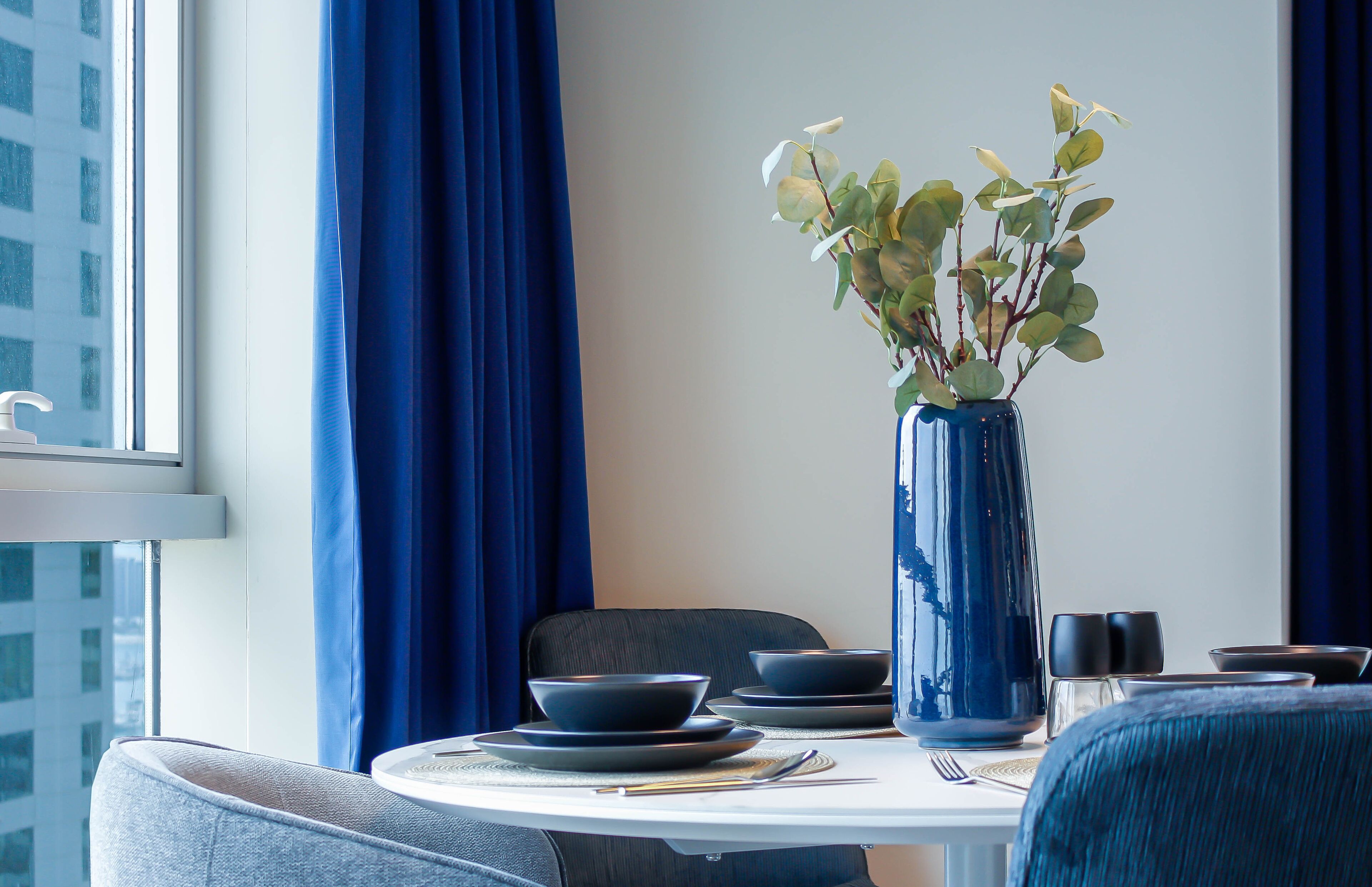 A dining table with a vase of green leaves, a bowl, and a cup.