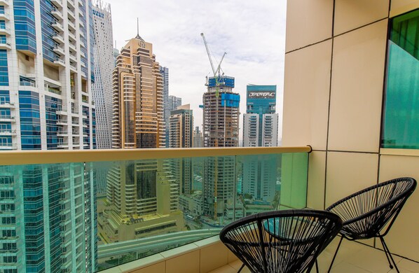 A balcony with two black chairs, overlooking a cityscape with high-rise buildings and a construction crane.