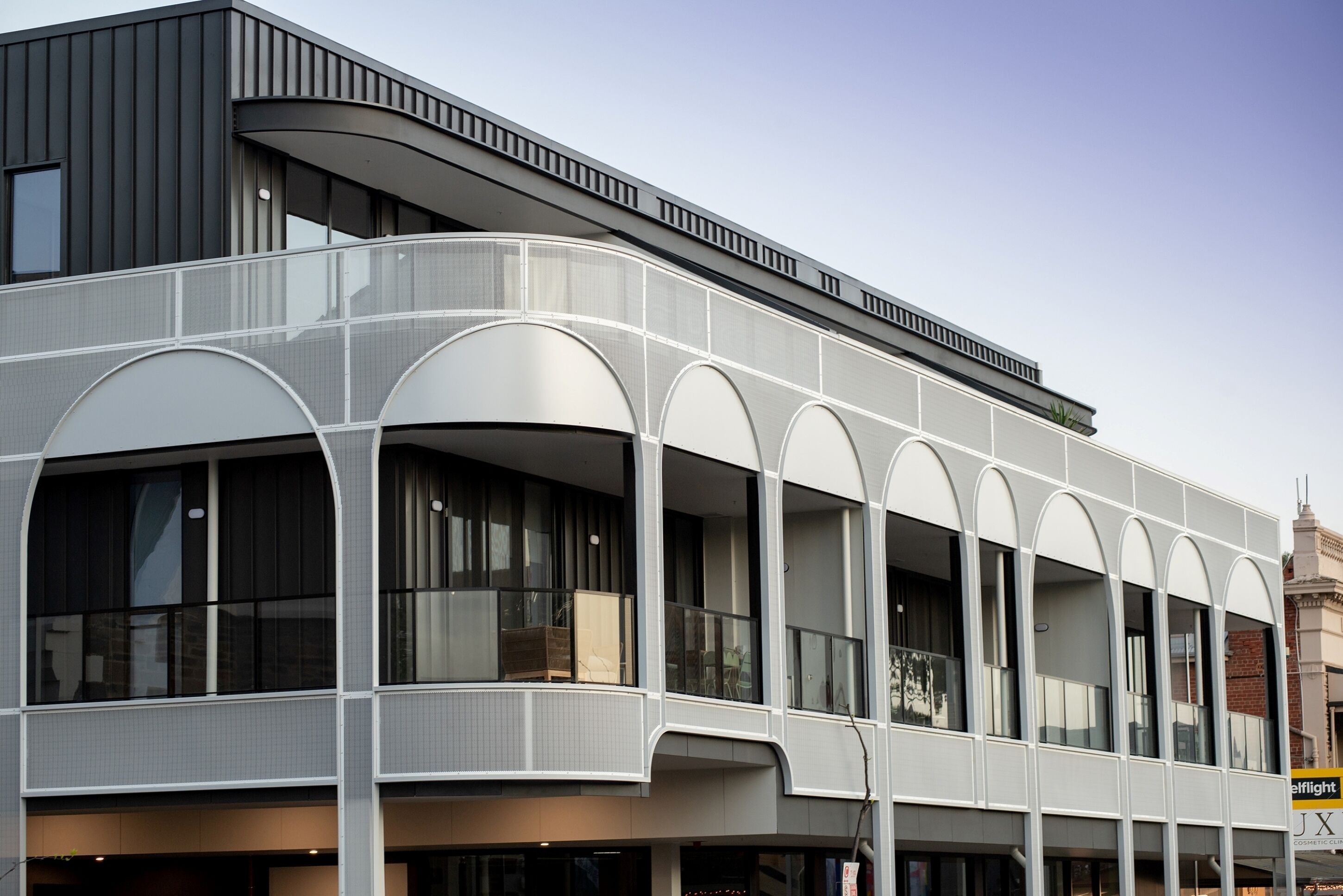 A modern building with a curved facade, large windows, and a balcony area.
