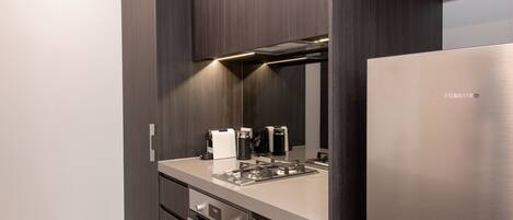A modern kitchen with dark wood cabinetry, a stainless steel refrigerator, a built-in oven, and a coffee machine.