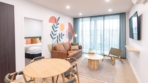 A modern living room with a sofa, a round coffee table, a TV mounted on the wall, and a large window with curtains. - Grow at Goodwood (Goodwood)