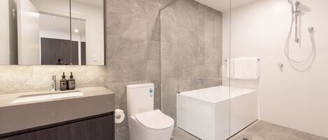 Une salle de bain moderne avec une douche à parois de verre, des toilettes blanches et un grand lavabo surmonté d’un miroir.