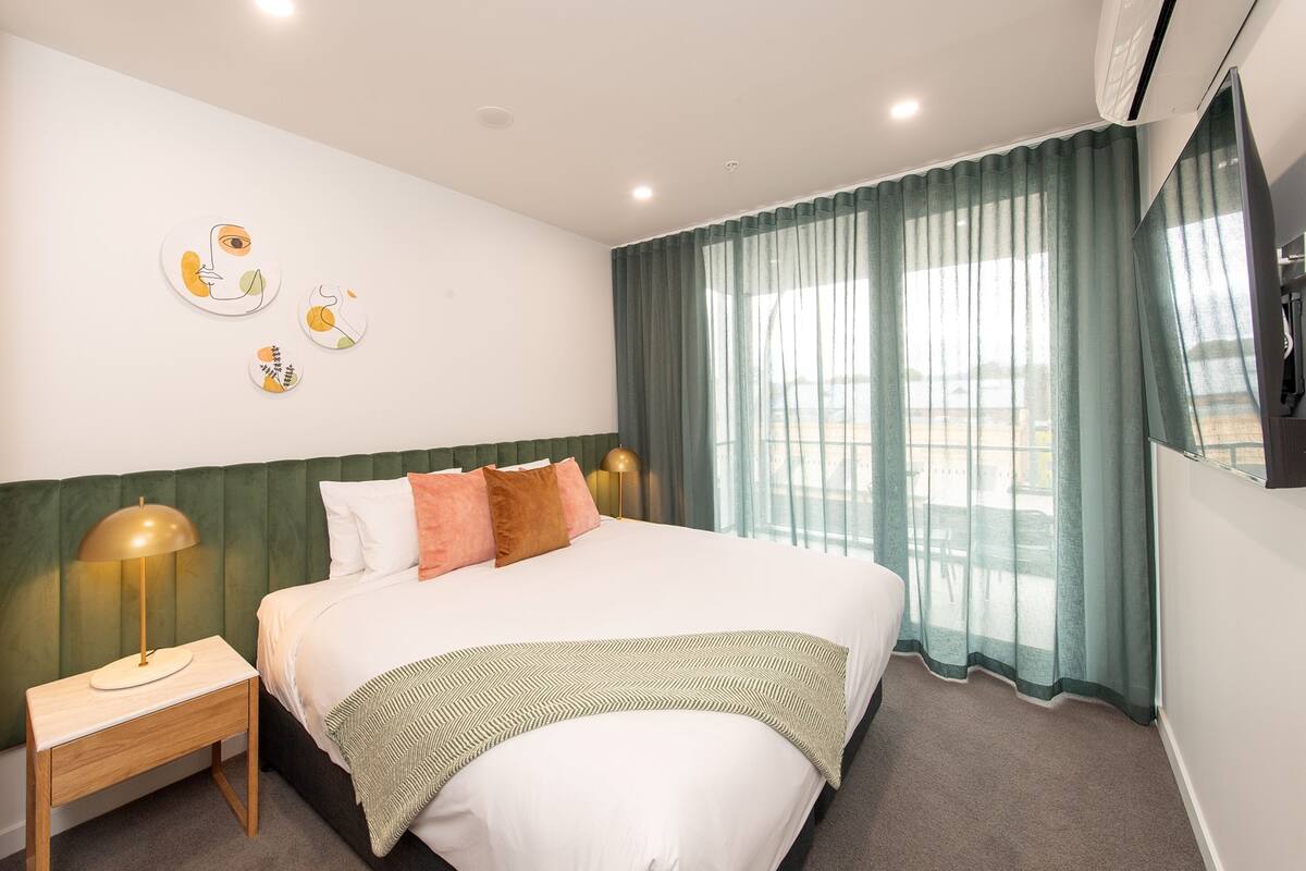 A neatly arranged hotel room with a large bed, a bedside table, a lamp, and a wall-mounted TV.