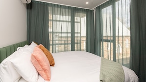 A hotel room with a large bed, green curtains, and a view of a brick building. - Grow at Goodwood (Goodwood)