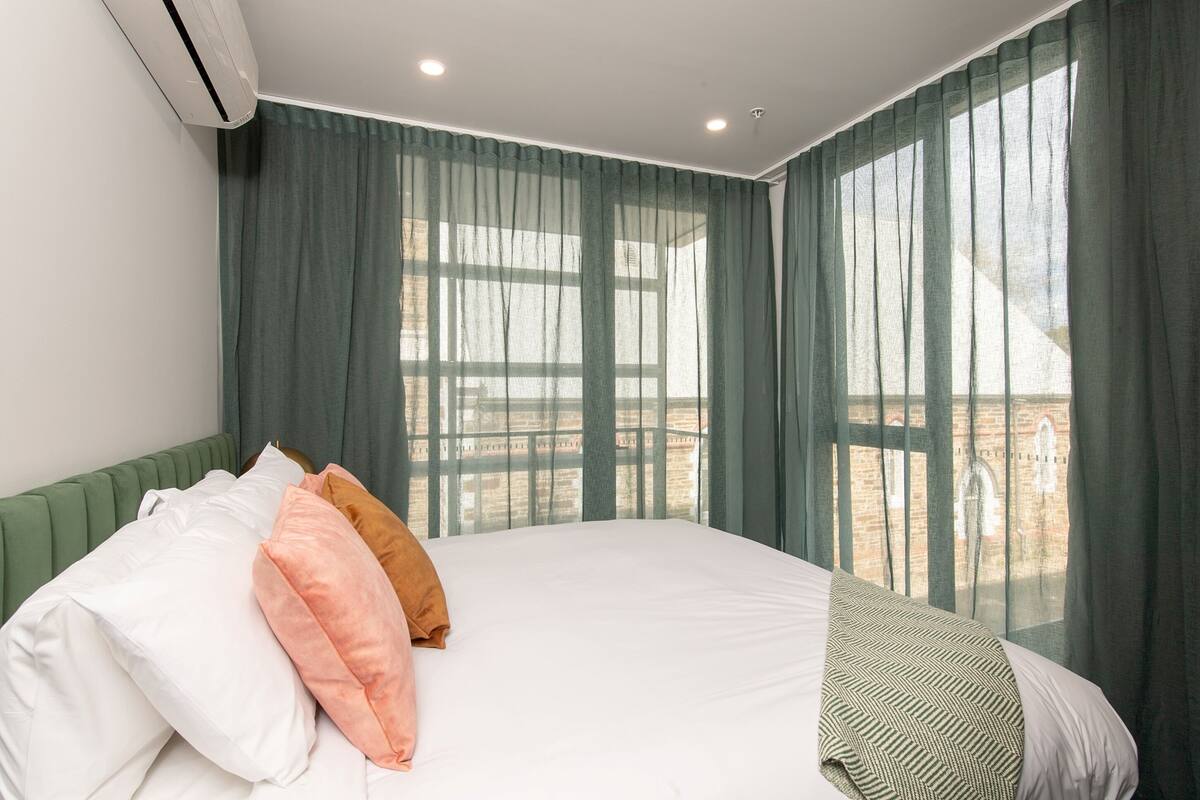 A hotel room with a large bed, green curtains, and a view of a brick building.