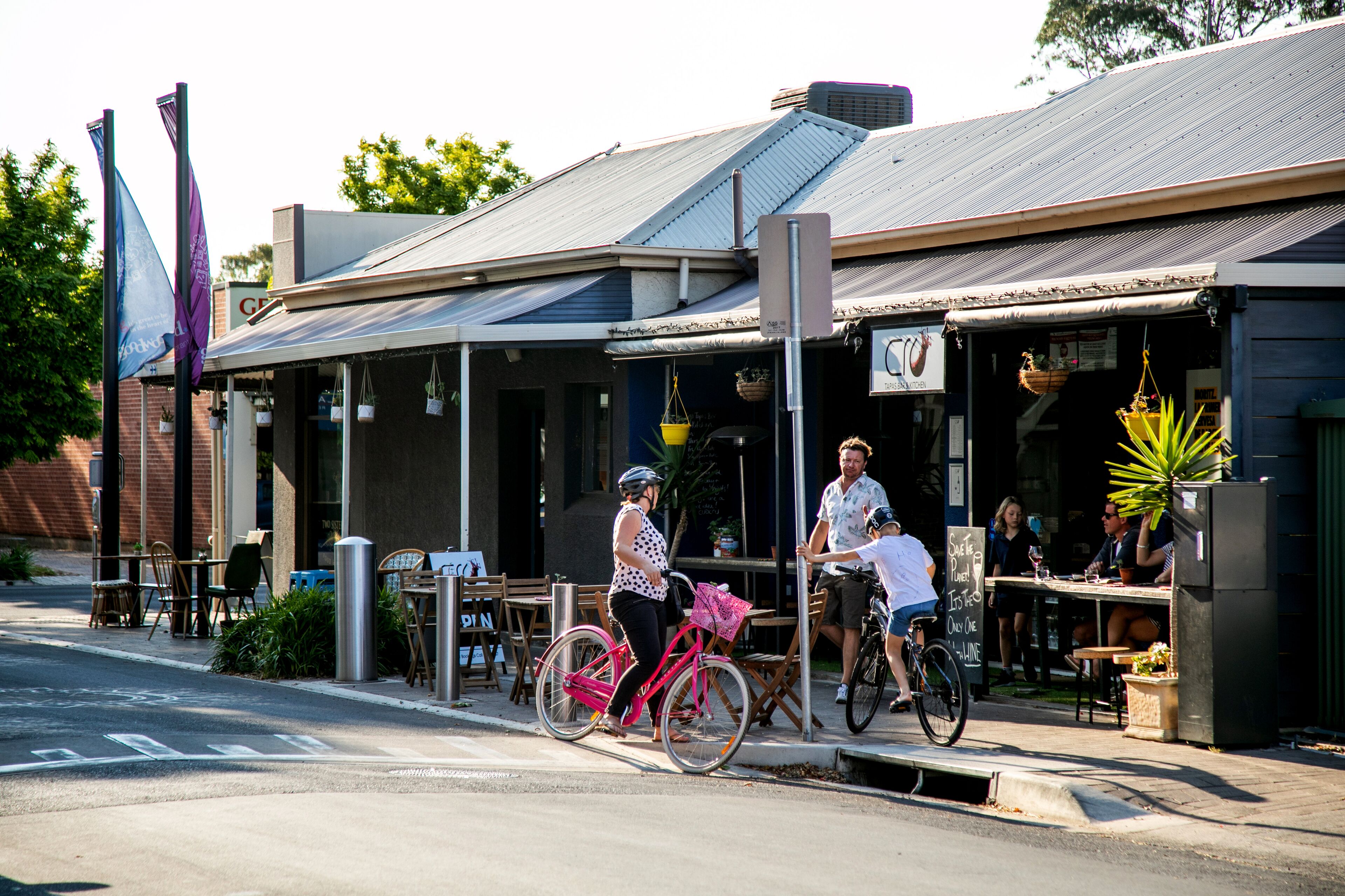 A street with outdoor seating at a cafe, a pink bicycle, and a person riding a bike.