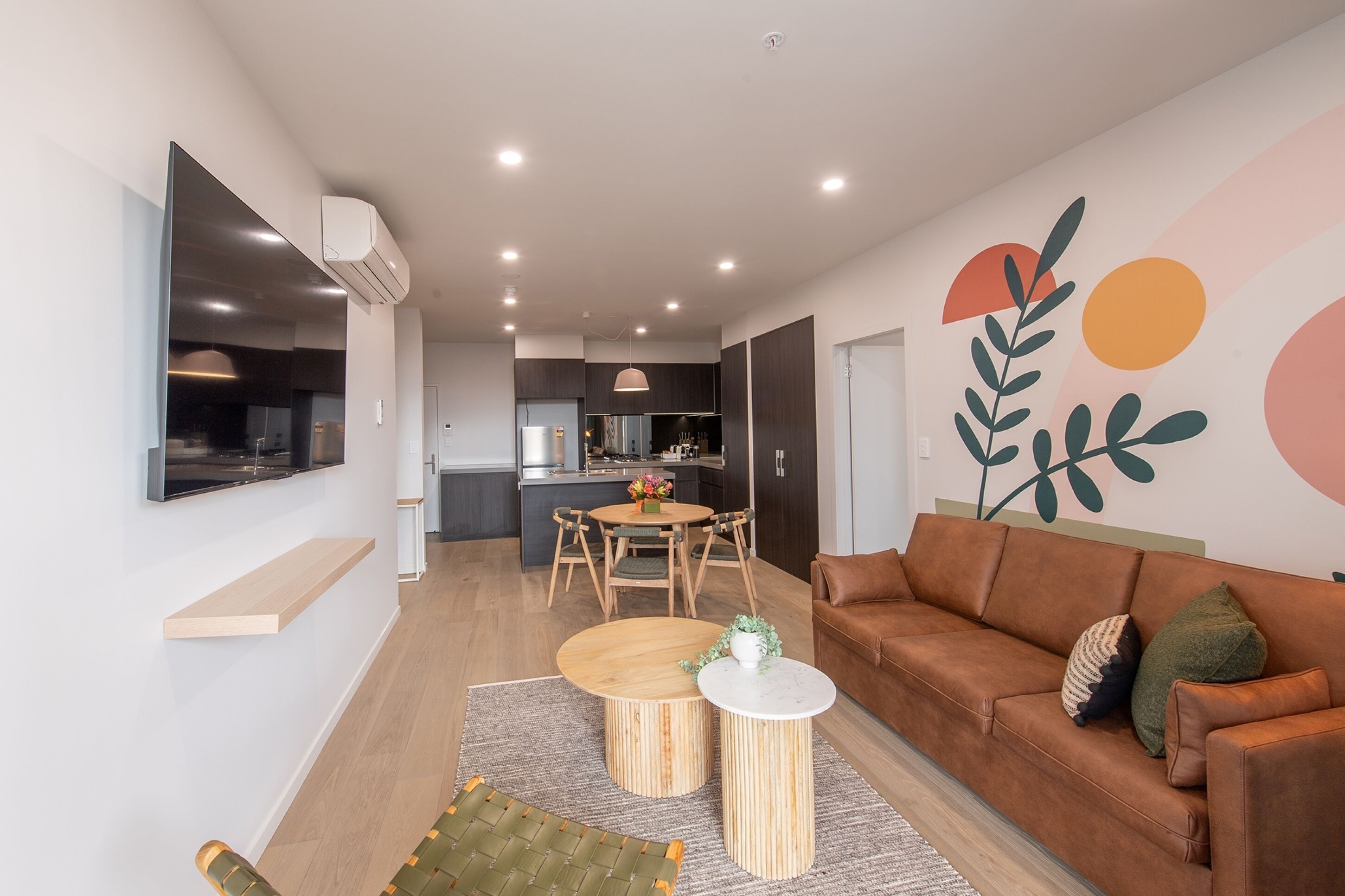 A modern living room with a brown leather sofa, a round wooden coffee table, and a TV mounted on the wall.