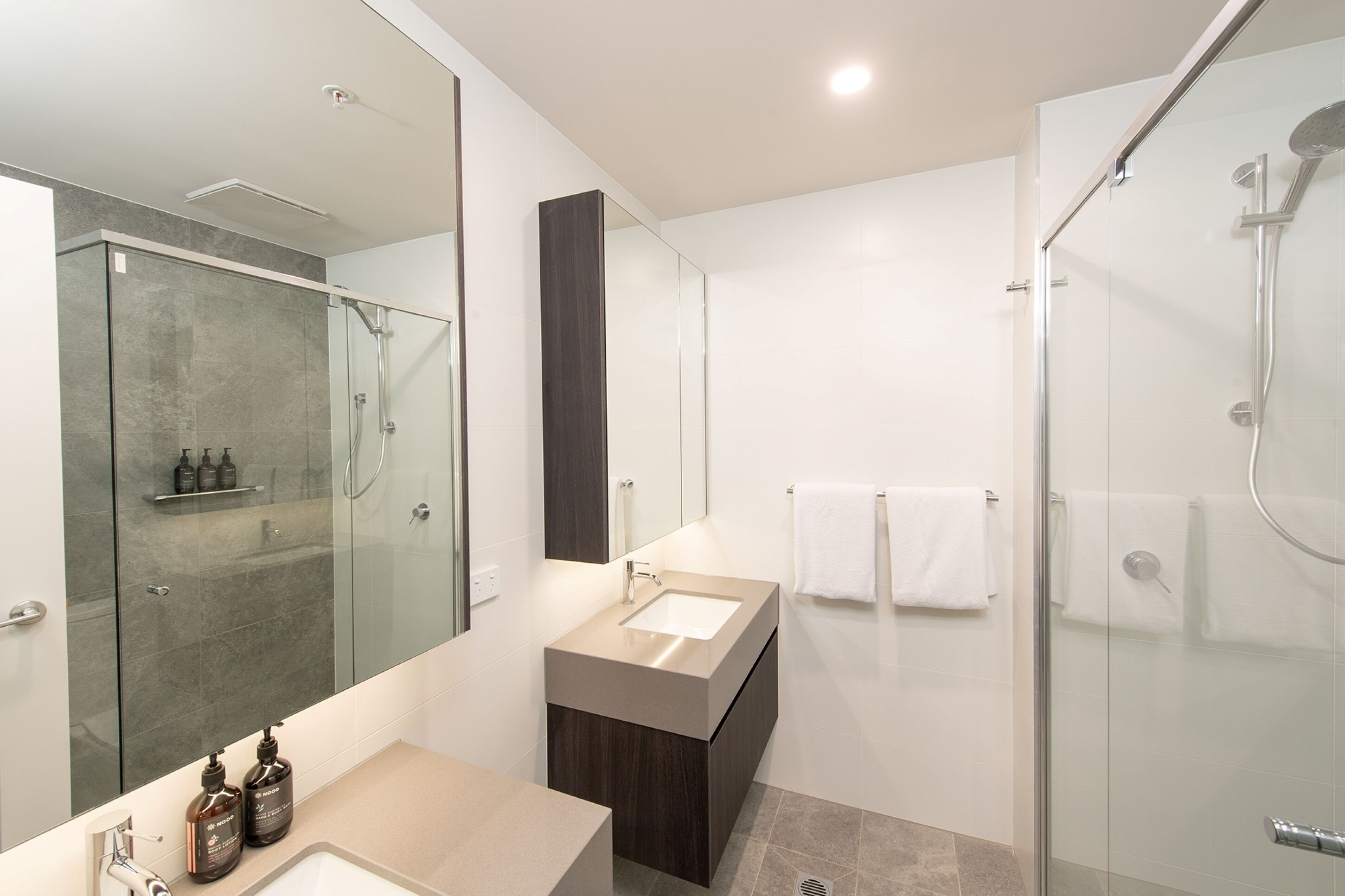 A modern bathroom with a glass-enclosed shower, a vanity with a sink, and a large mirror.