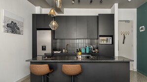 A modern kitchen with dark cabinetry, a central island with stools, a microwave, and a kettle. - The Duke 905 (Cape Town)