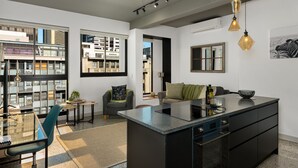 A modern kitchen with a central island, a dining area with a glass table, and a view of the cityscape through large windows. - The Duke 905 (Cape Town)