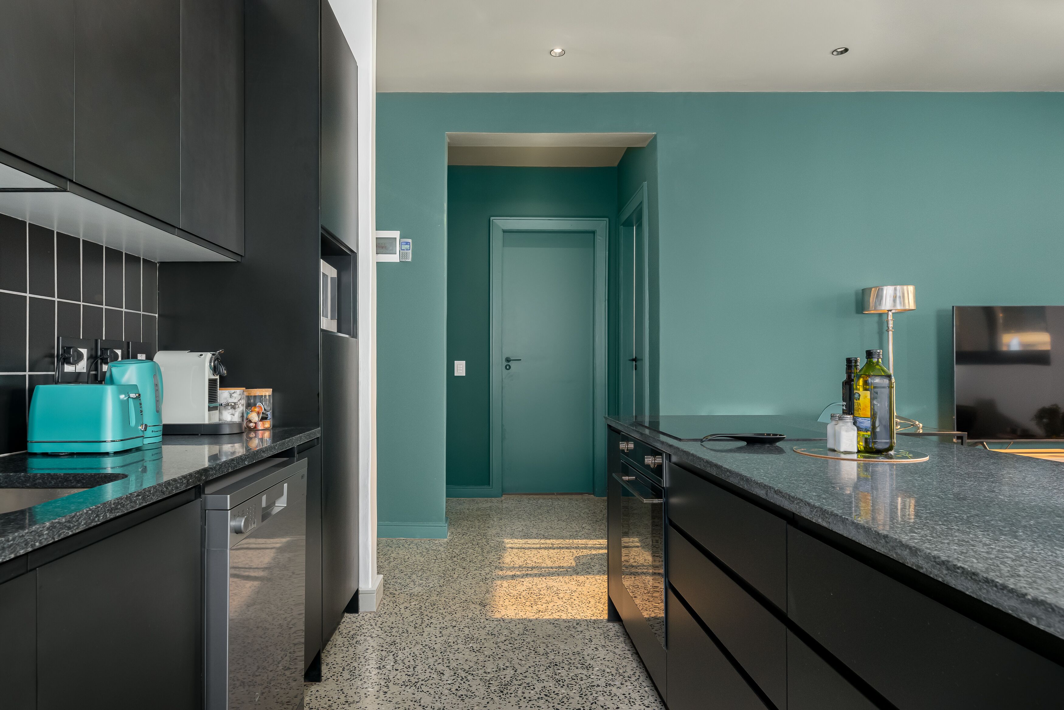 A modern kitchen with dark cabinetry, a teal accent wall, and a granite countertop.