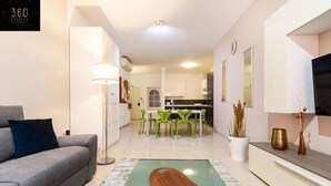 A modern living room with a grey sofa, a wooden coffee table, and a dining area with green chairs. - Designer, fully equipped APT, just off Tower Road (Tas-Sliema)