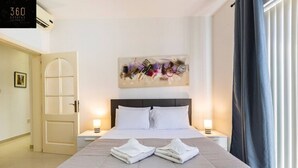 A hotel room with a bed, two bedside tables with lamps, a painting on the wall, and a door. - Designer, fully equipped APT, just off Tower Road (Tas-Sliema)
