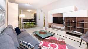 A modern living room with a grey sofa, a glass coffee table, and a flat-screen TV mounted on the wall. - Designer, fully equipped APT, just off Tower Road (Tas-Sliema)