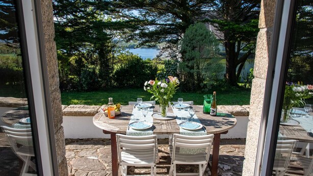 Un espacio de comedor al aire libre con una mesa preparada para cuatro personas, rodeado de muros de piedra y vistas al mar.