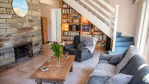 Una sala de estar acogedora con chimenea, una mesa de centro de madera, un sofá y una estantería llena de libros.