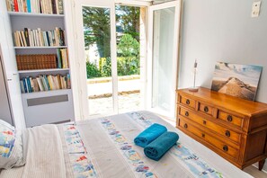 Una camera da letto con un letto, una cassettiera, una libreria e una porta scorrevole in vetro che dà su uno spazio esterno.