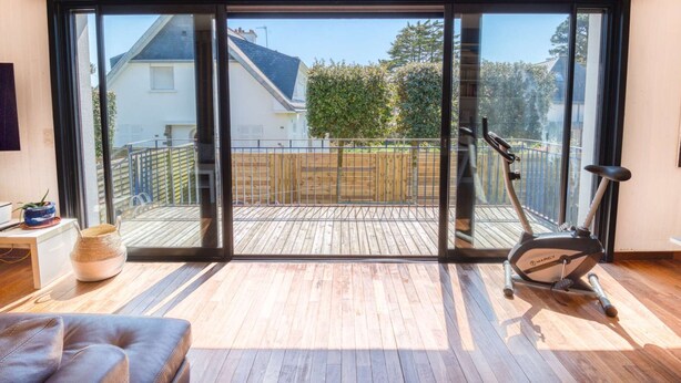 Een ruim balkon met een houten terras, een hometrainer en uitzicht op een woonwijk.