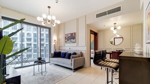Un salon moderne avec un canapé, un coin repas comprenant une table et des chaises, et une grande fenêtre donnant sur un immeuble.