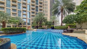 Une piscine aux motifs à carreaux bleus, entourée de palmiers et bordée d’un immeuble de grande hauteur doté de balcons.