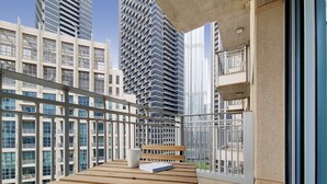 Un balcon avec un banc en bois et une tasse blanche, d’où l’on peut admirer les immeubles modernes qui s’élèvent dans le paysage urbain.