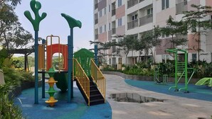 Un parque infantil con juegos de colores, una fuente de agua y un edificio al fondo.