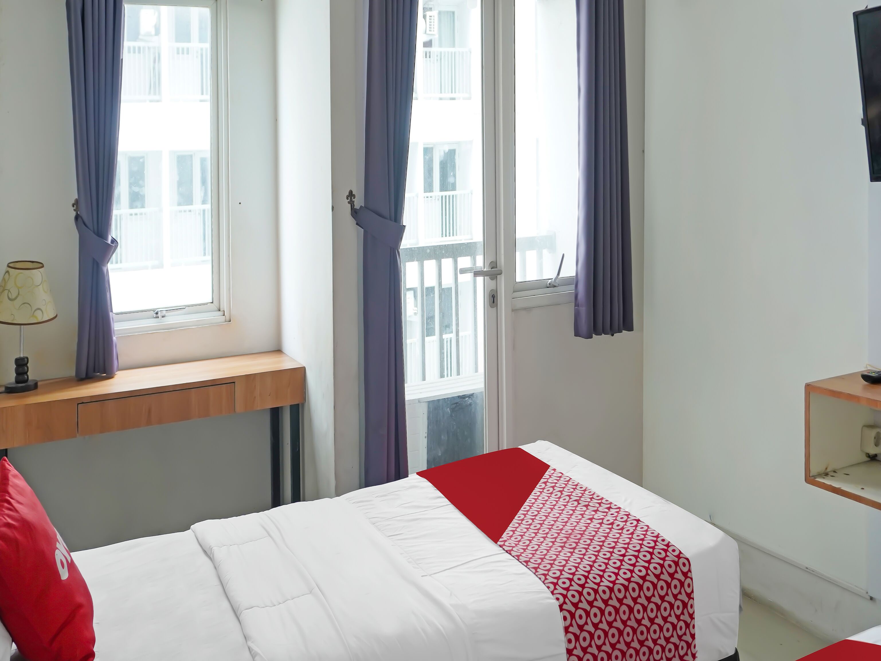 A hotel room with a bed, a desk, a chair, and a window with curtains.