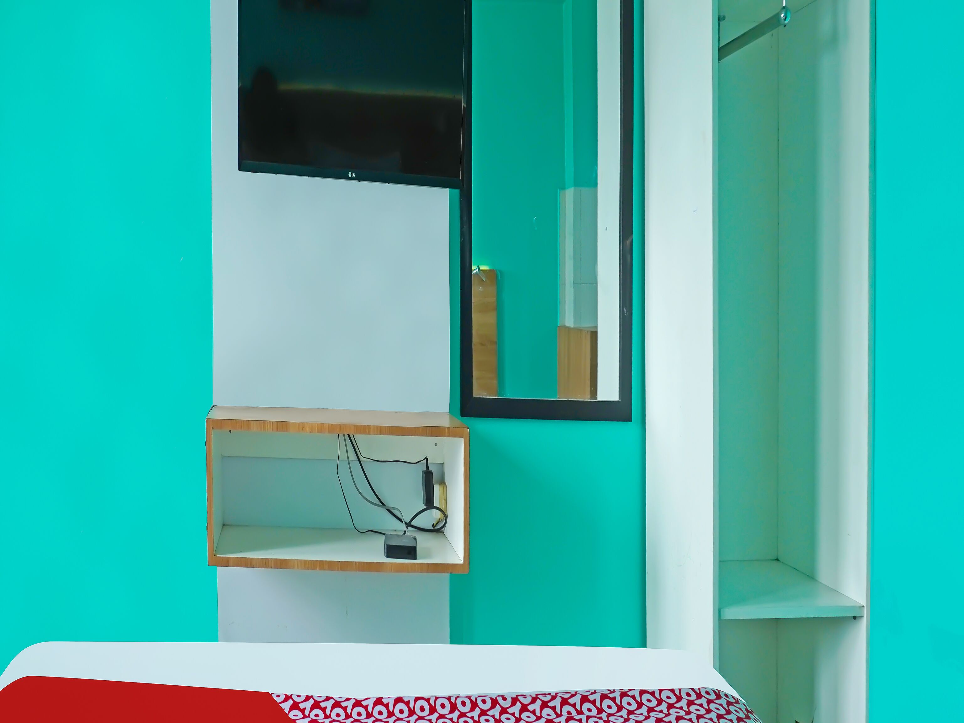 Quarto com paredes verde-água, uma estante branca com régua de tomadas e um espelho refletindo parte do quarto.