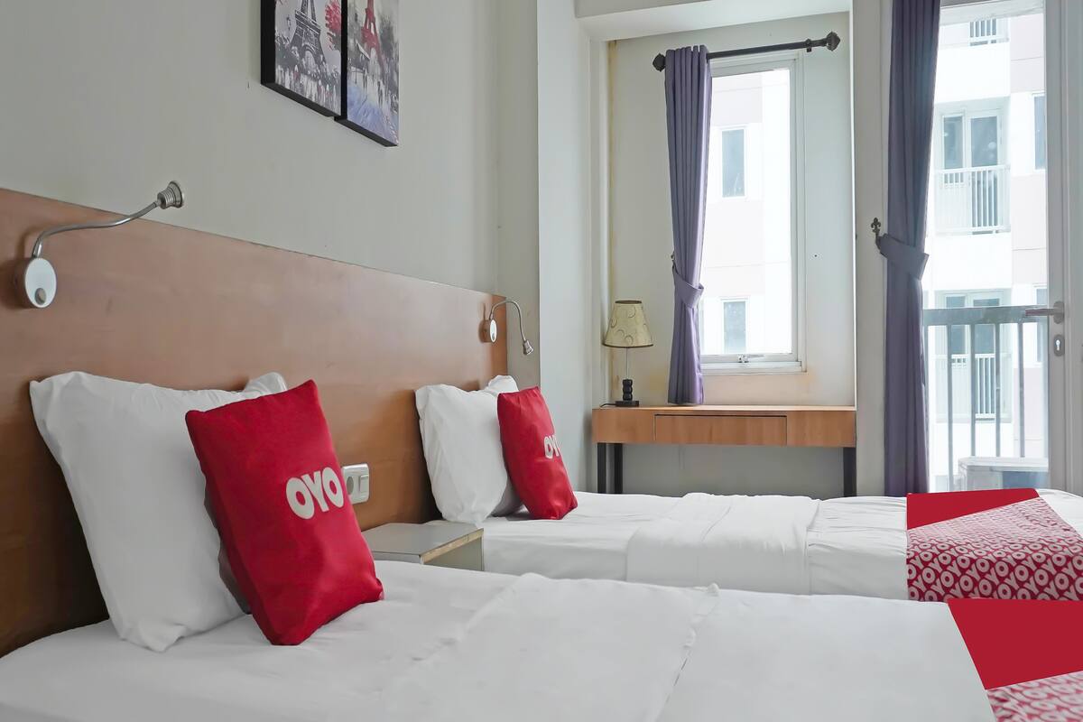 Quarto de hotel com duas camas, uma cabeceira de madeira, mesa de cabeceira, abajur e janela com cortinas.