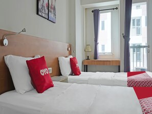 A hotel room with two beds, a wooden headboard, a nightstand, a lamp, and a window with curtains.