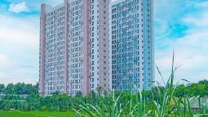Un edificio residencial alto con múltiples balcones, rodeado de abundante vegetación y un cielo despejado.