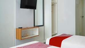 Habitación de hotel con cama, televisor montado en la pared, mesita de noche de madera y armario.