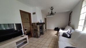 Een woonkamer met een flatscreen televisie op een houten standaard, een stenen open haard, een witte bank met een zwart kussen en een kroonluchter.