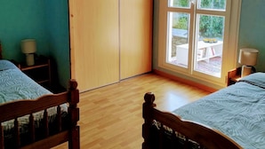 Een slaapkamer met twee houten bedden, een kledingkast en een groot raam met uitzicht op het omliggende landschap.