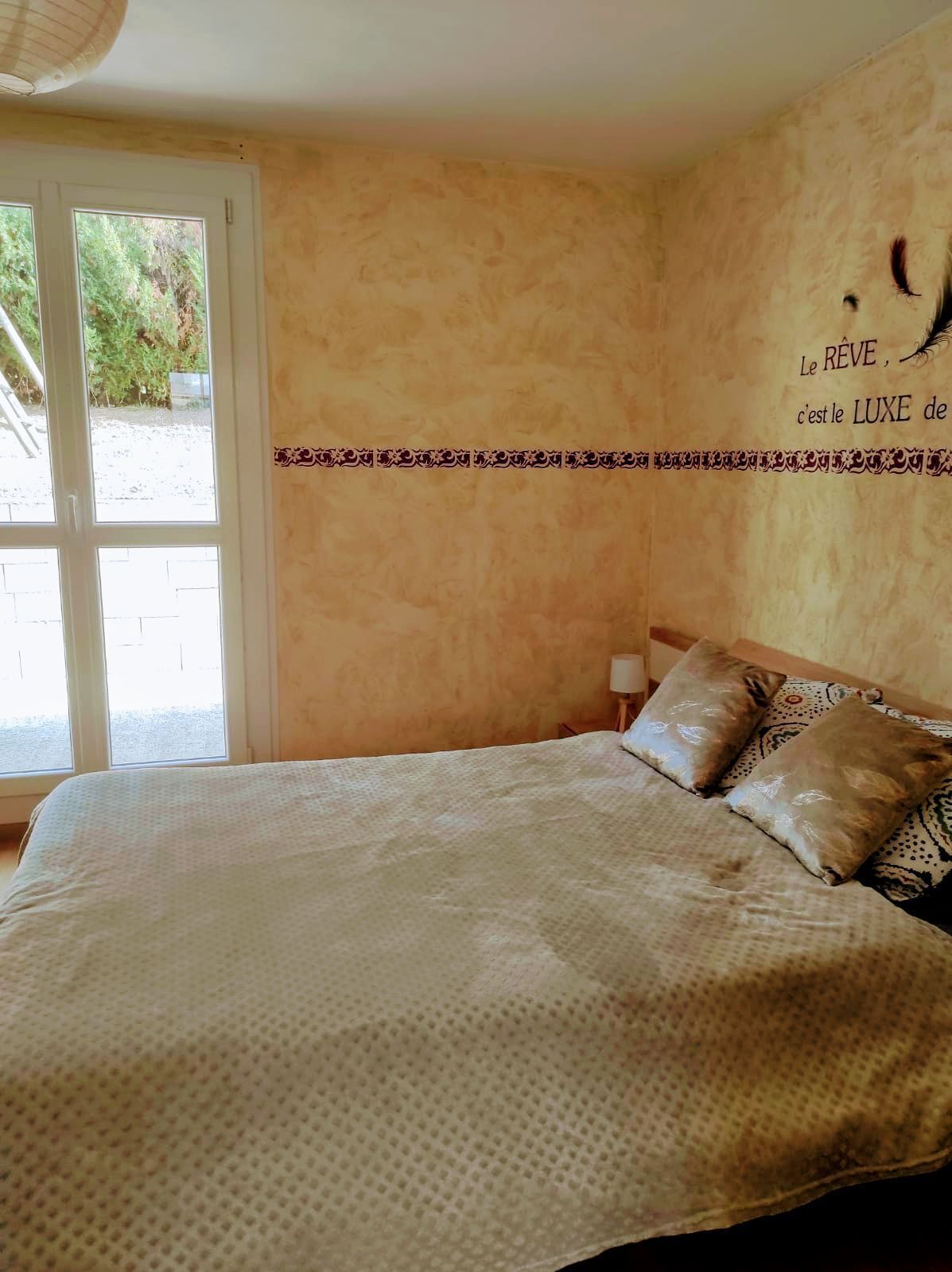 Een slaapkamer met een bed, kussens, een wand met decoratieve rand en een raam met uitzicht op groen.
