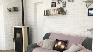 Un salon avec un mur en briques blanches, un canapé avec des coussins, une petite table avec un panier et une bibliothèque remplie de livres et d’une horloge.