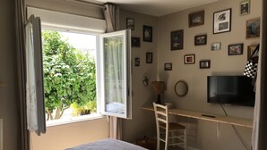 Une chambre à coucher avec un lit, un bureau, une chaise, une télévision et une fenêtre avec des rideaux.