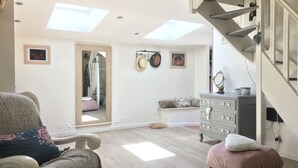 Une pièce spacieuse avec un plafond haut, des fenêtres de toit, un escalier, un lit recouvert d’une couverture rose, une commode et un miroir.