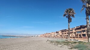 A coastal hotel with multiple-story buildings, a sandy beach, and palm trees. - Apartment in Almerimar with Pool & Beaches (Almeria)