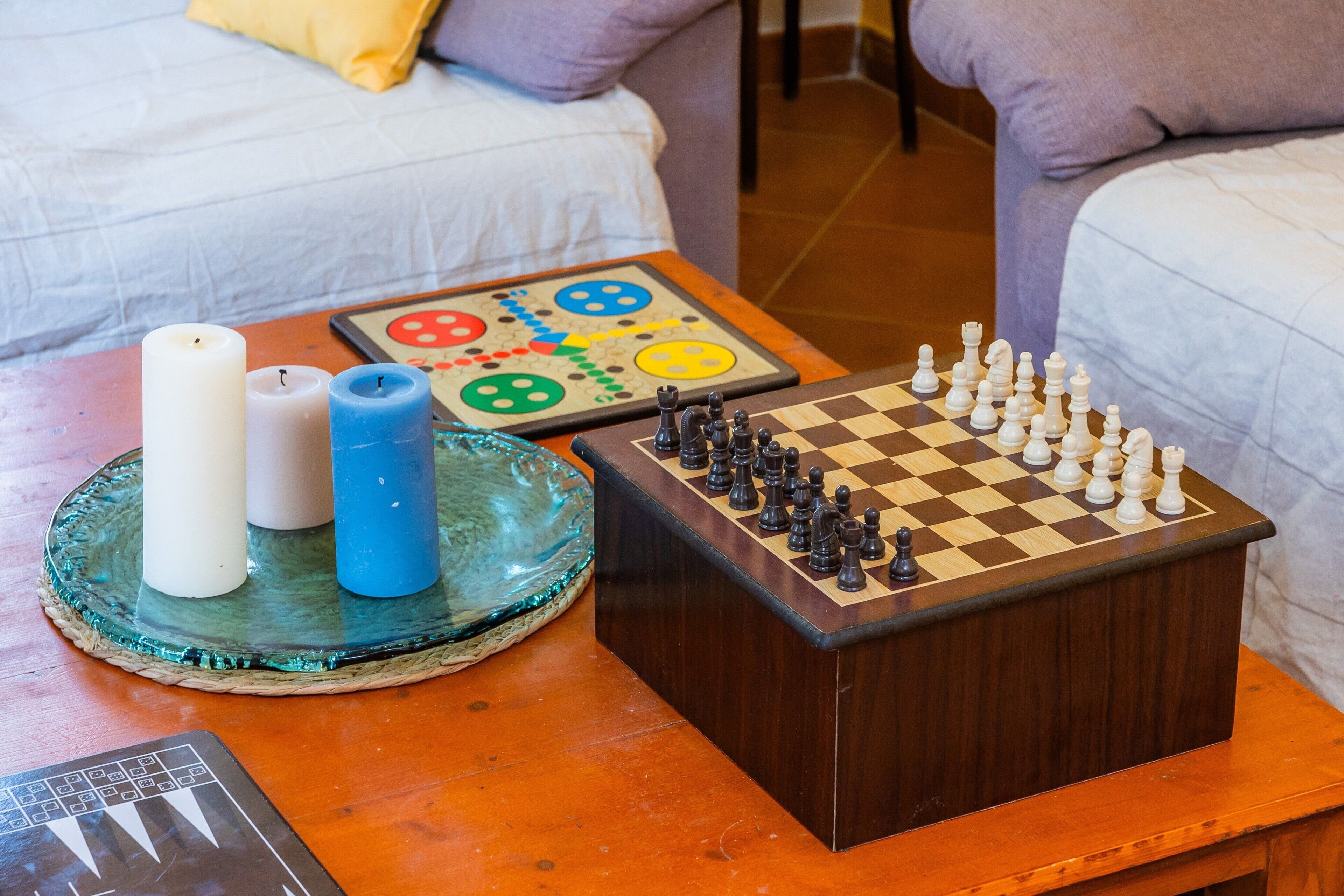 A chessboard on a wooden table with candles and a board game nearby.