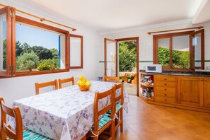 A dining area with a table, chairs, and a view through open windows.