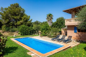 Une piscine entourée de chaises longues, un bâtiment en pierre doté d’un balcon, et une végétation luxuriante.