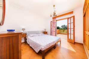 Une chambre à coucher avec un lit, une commode en bois, une table de chevet, une lampe et une vue sur l’extérieur.