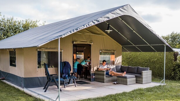 A covered outdoor seating area with a sofa and chairs, a dining table, and a tent-like structure.
