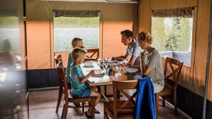 A family dining at a wooden table with a view of greenery outside.